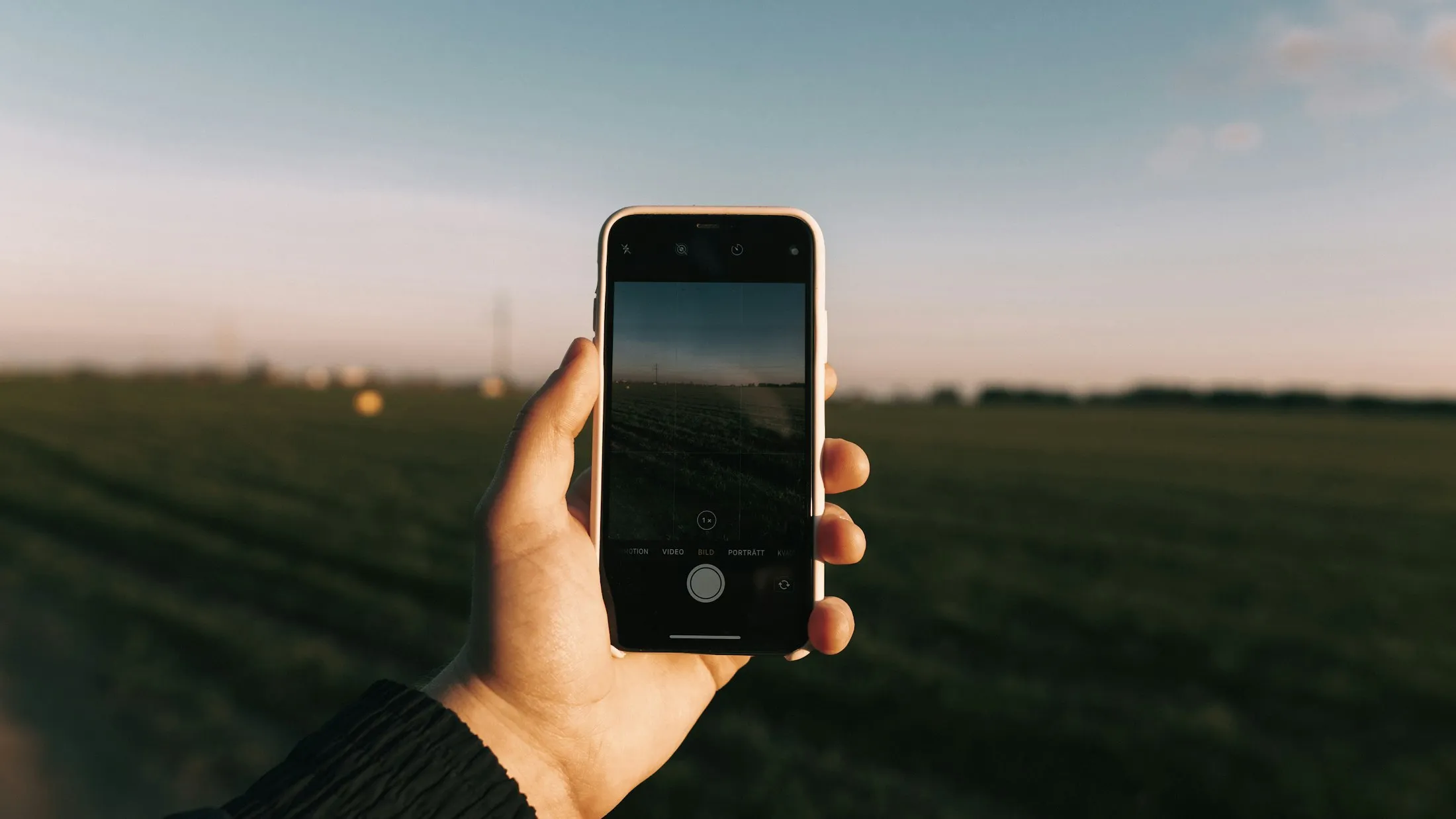 A hand holding up a phone against a field at dusk