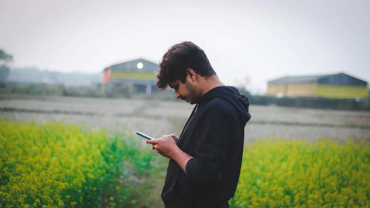 A farmer checks his phone at the edge of a field